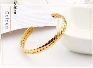 Detailed macro view of golden stainless steel wheat ear open cuff bracelet on white background