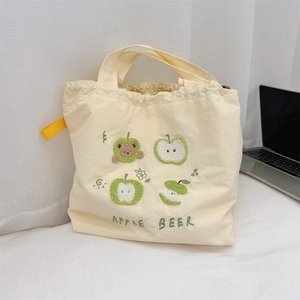 Detail of cream canvas tote bag featuring apple embroideries and yellow webbing handle