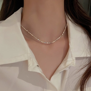 Close-up of faceted silver beads on a chain necklace reflecting light on the collarbone