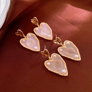 Detailed macro view of heart earrings with gold wavy frames, dried leaves and pearls