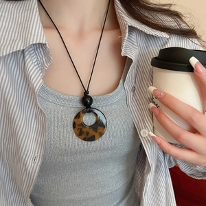 Detail shot of leopard print pendant on a black cord necklace worn by a model