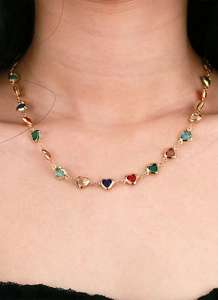 Detail of a gold choker necklace featuring colorful heart-shaped zircon gemstones on skin