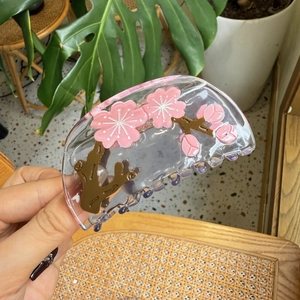 Detailed close-up of a clear acetate hair claw clip featuring pink cherry blossom patterns
