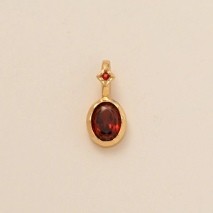 Gold pendant with oval red gemstone and star detail on light textured background