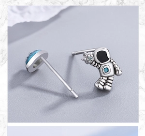 Macro view of silver astronaut stud earrings with blue planet and sparkling star detail