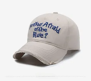 Detail of beige baseball cap featuring blue embroidery and distressed frayed edge brim