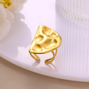 Close-up of golden open ring with irregular hammered texture on a white ceramic plate