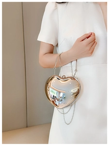 Detail of silver heart-shaped acrylic bag with metal chain shown on a white dress