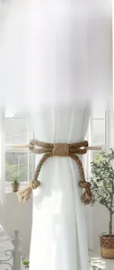 Detail of hand-woven cotton rope curtain tieback with natural wooden stick fastening