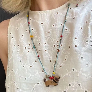Detail of beaded cord necklace with a brown dachshund dog pendant on white lace dress
