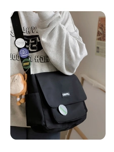 Detail of black canvas messenger bag featuring decorative badges and a cute plush pendant
