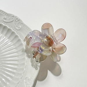 Haarklammer aus Acetat in Blumenform mit Perlglanz-Farbverlauf auf weißem Keramikteller