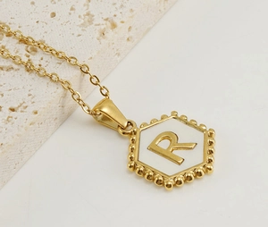 Macro shot of 18K gold hexagon pendant with shell inlay and R initial detail