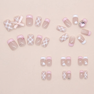 Detail of pink and white press-on nails with plaid patterns, bows and rhinestones