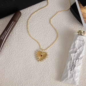 Macro detail of 18K gold stainless steel necklace with red heart pendant and crystals