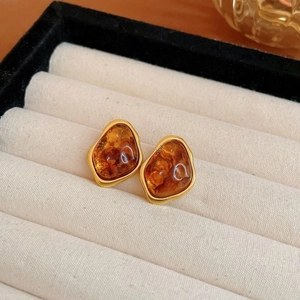 Close-up of irregular amber studs with gold trim inside a beige velvet jewelry box