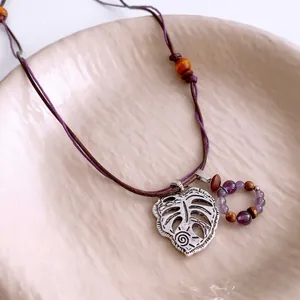 Retro Monstera leaf pendant necklace with purple beads and brown wood on braided cord