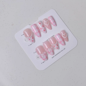 Detail of pink almond press-on nails with 3D bows, pearls and plaid strawberry design