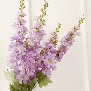 Artificial purple delphinium flowers with green leaves against a clean white background