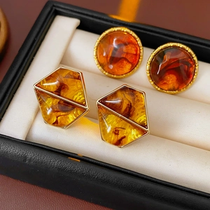 Close-up of golden geometric resin earrings with amber texture on a white jewelry cushion