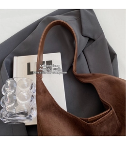 Detail of brown suede tote bag with smooth leather strap on grey blazer and book