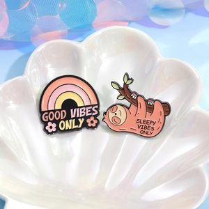 Cartoon enamel pins with Good Vibes and Sleepy Vibes text on a white shell plate
