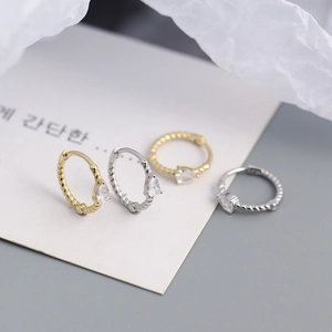 Close-up of twisted hoop earrings with drop-shaped zircon in gold and silver finishes