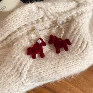 Detail of red flocked horse earrings with white pearl beads on cozy knit background