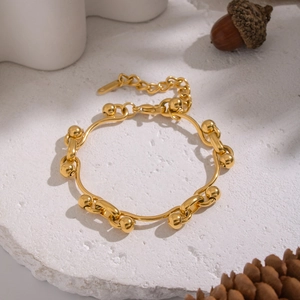 Detail of 18K gold-plated stainless steel ball chain bracelet on white stone surface