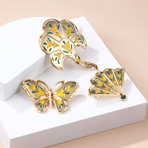 Elegant gold-tone butterfly and fan enamel brooches on a minimalist geometric display