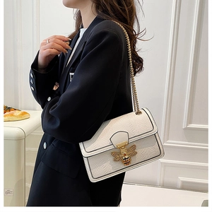 Detail of white snake-textured crossbody bag with golden bee buckle and metal chain strap