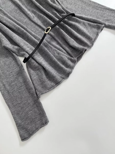 Detail of grey knitted sweater featuring fine texture and a slim black belt with gold buckle