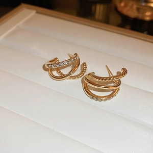 Detail of layered gold-plated C-shaped earrings with rhinestones on a white tray