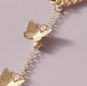Vue détaillée d'une chaîne dorée avec des pendentifs papillons sur un fond de couleur lilas
