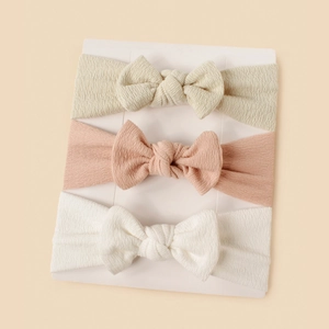 Three-piece set of ribbed baby headbands featuring bows in beige, pink, and white