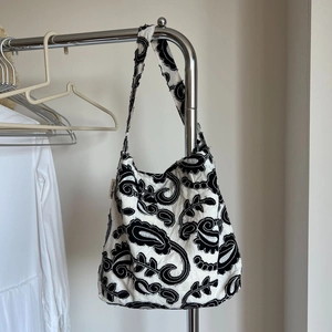 Detail of floral paisley embroidery and brand tag on a white canvas shoulder bag