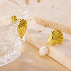 Close-up of golden shell earrings with white pearls on a textured stone surface