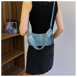Detail of blue denim shoulder bag with silver metallic studs shown on a model