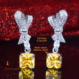 Macro detail of radiant cut yellow diamond earrings with bow design and 3cm size labels