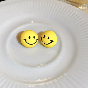 Close-up of yellow cartoon smiley face earrings with silver needle on white ceramic