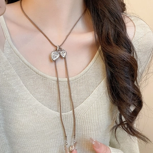 Detail of silver heart pendants on long brown cord necklaces worn over a cream sweater