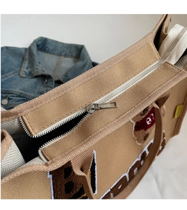 Detail of khaki canvas tote featuring bear embroidery and premium metal zipper closure