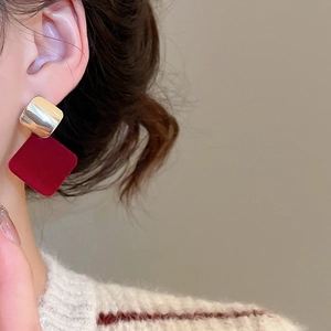 Détail d'un mannequin portant des boucles d'oreilles carrées en velours bordeaux et or