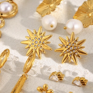 Macro shot of 18K gold plated earrings featuring pearls and zircons on beige fabric