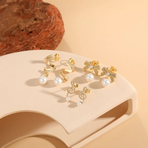 Detailed close-up of gold zircon pearl earrings featuring ribbon and musical note designs