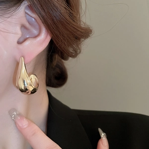 Close-up of golden curved teardrop earring worn with a professional black blazer