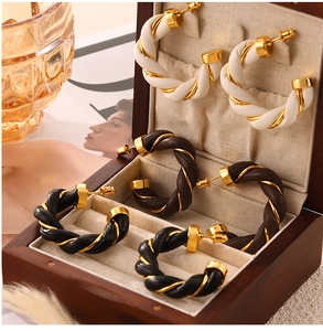 Close-up of twisted leather and gold metal hoop earrings in white, brown and black
