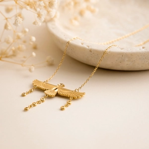 Detail of 18K gold-plated eagle necklace with wings and metal bead tassels on a tray