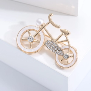 Detailed close-up of a gold bicycle brooch with white enamel, pearls, and crystals