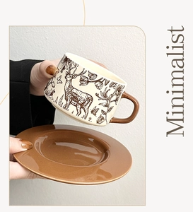 Detail of a ceramic coffee mug with hand-painted brown elk and a minimalist saucer